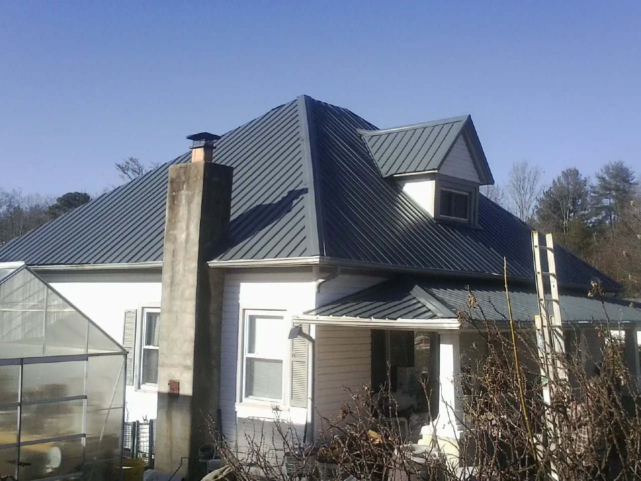 Dark blue standing seam metal roof on a white farmhouse with dormer — Slate & Tile Roof Repair by Roofing Brothers in Cherry Valley