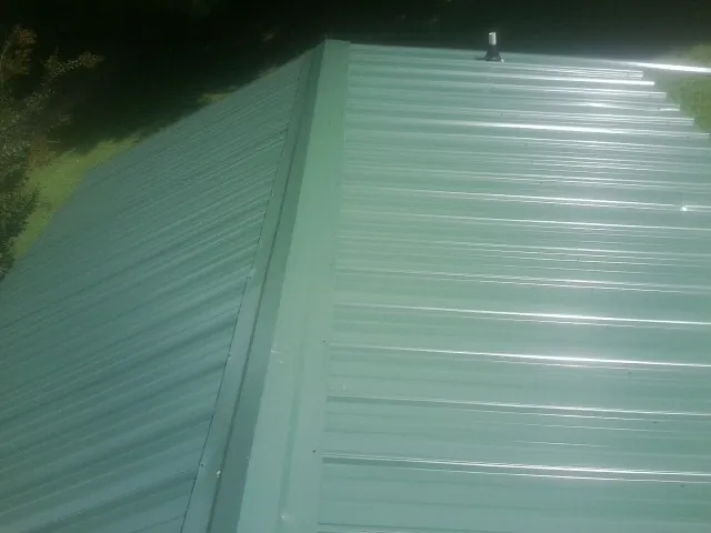 New green metal panels meeting at the ridge of a roof — Flat Roof Repair work by our crew in Cherry Valley