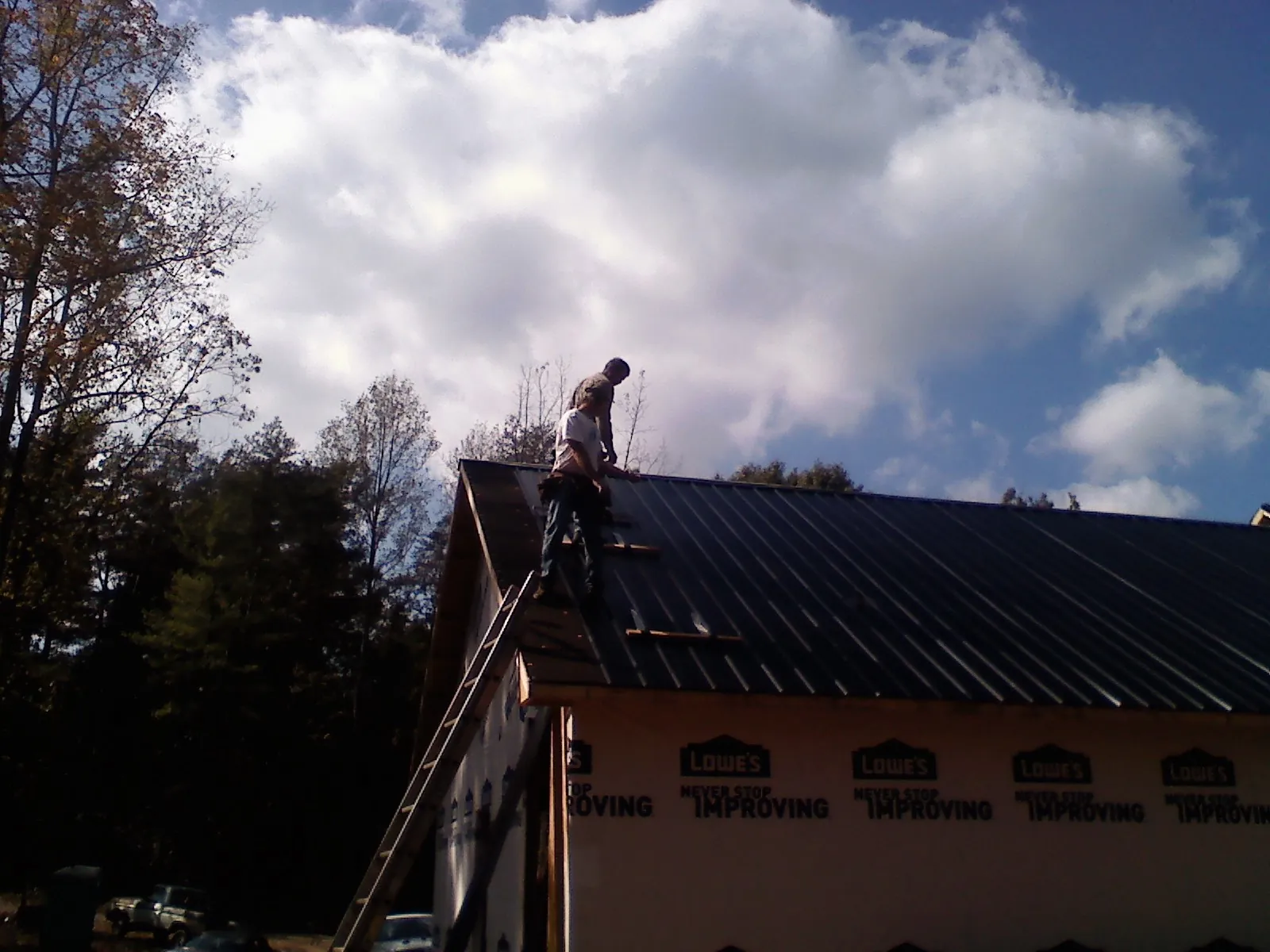 Roofer fastening dark metal panels high against a cloudy sky, from a Roof Inspection job in Cherry Valley