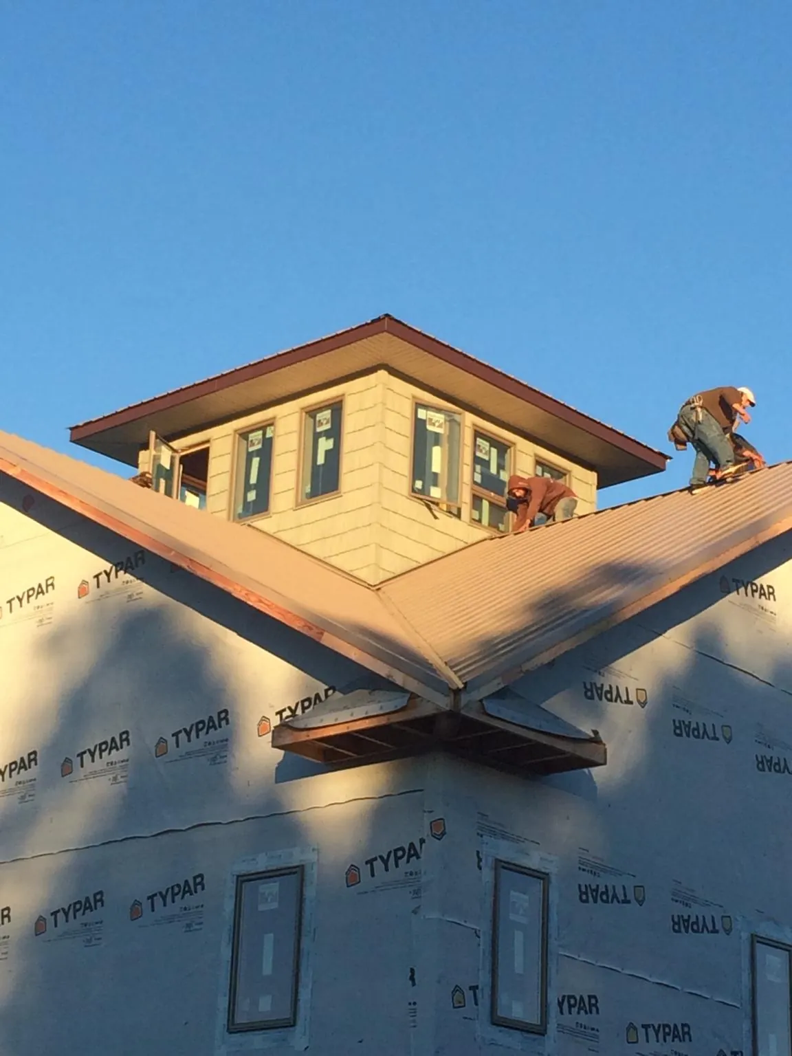 Roofers working around a rooftop cupola on a new metal roof at sunset — Roof Waterproofing in Cherry Valley by Roofing Brothers